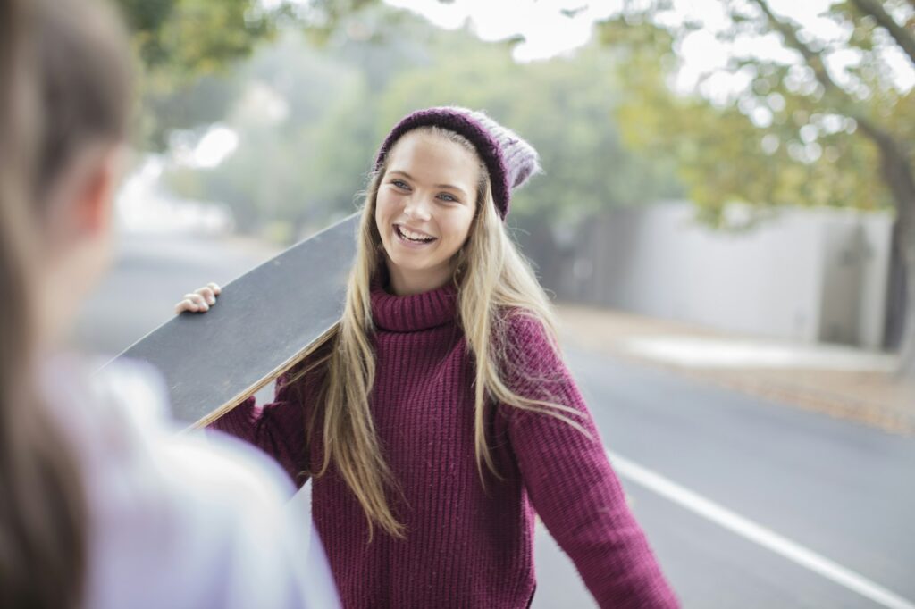 Teenage girl with a bright white smile holding a skateboard, representing Kids Smiles Pediatric Dentistry's teeth whitening services for teens in St. Louis